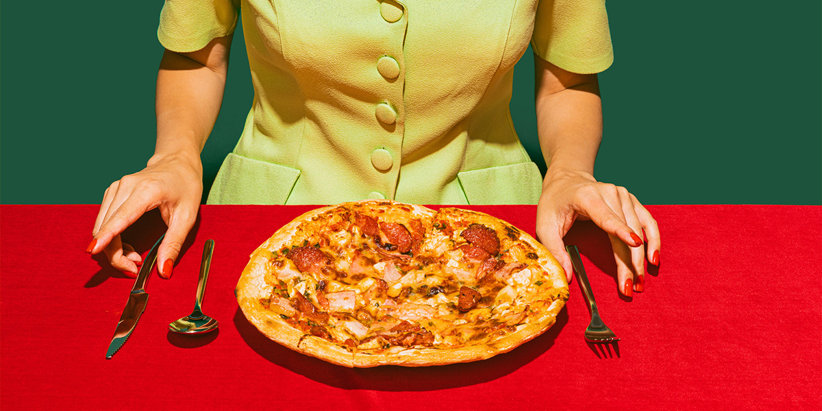 woman ready to eat pizza with silverware on a red table