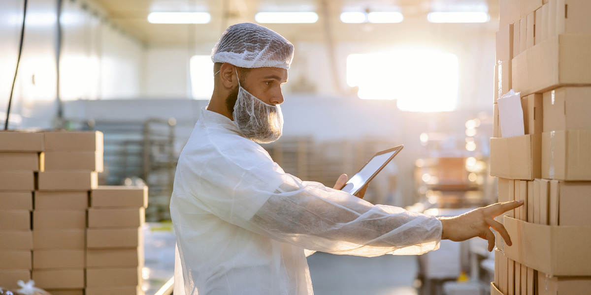 man in warehouse looking at boxes with hairnet on beard